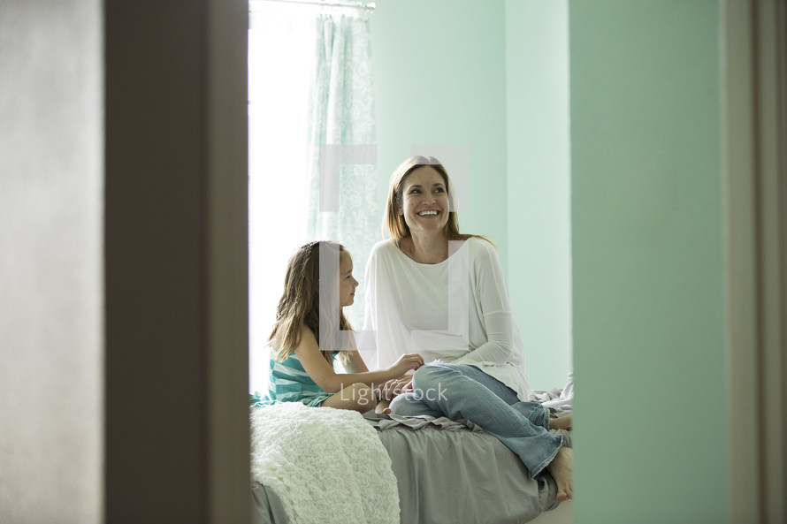 a mother and daughter talking while sitting on a bed 