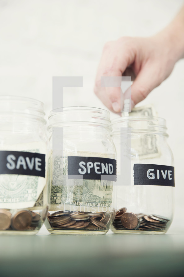 placing money in Give, Save, Spend money jars 
