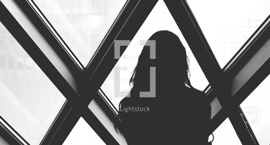 Silhouette of a woman looking out of diamond shaped windows.