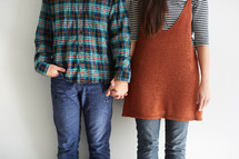 couple holding hands against white wall