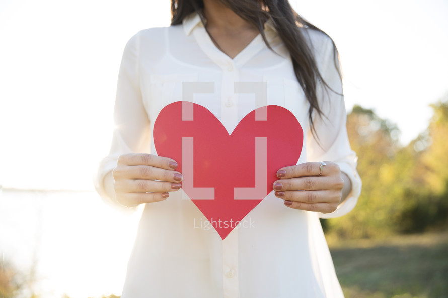 woman holding up a paper heart outdoors 