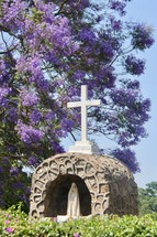 purple flowering tree over a statue of Mary 