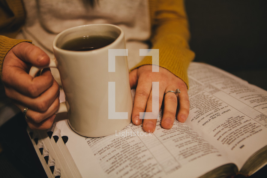 A woman holding a coffee cup and reading a Bible. 