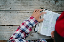 man reading a Bible outdoors at a picnic table 
