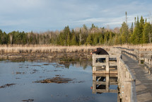 Man kneeling against a rail of a wooden bridge across a lake.