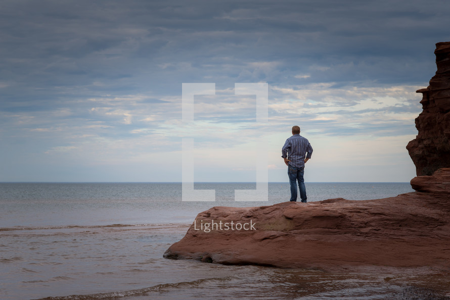 a man standing on rocks looking out at the ocean 