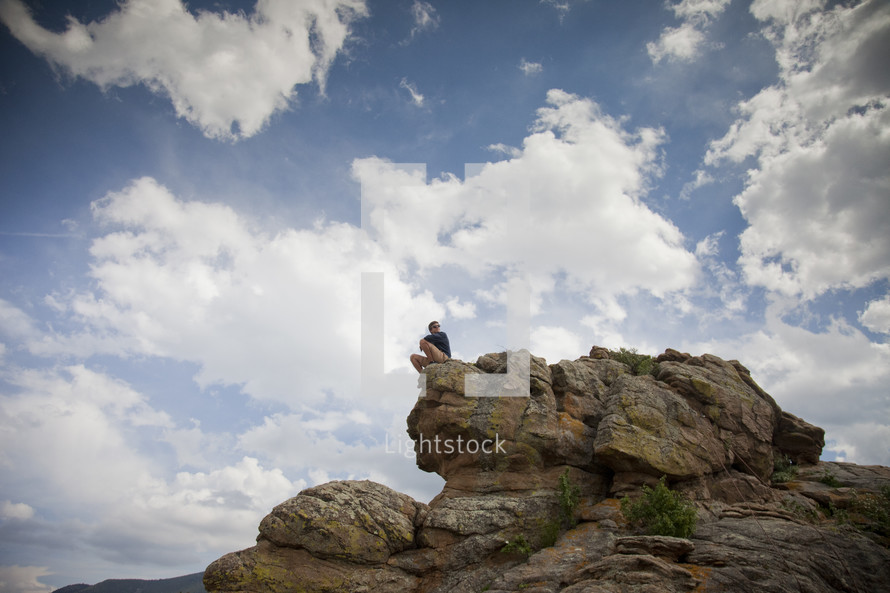 a man sitting at the edge of a large rock 