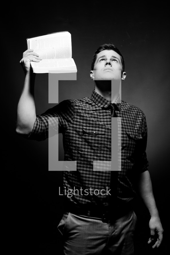 man holding up the pages of a Bible and looking to God for answers