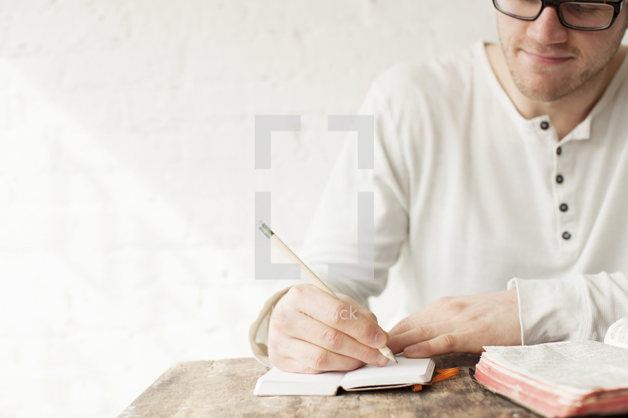 Man writing in a journal on a wooden desk with a Bible.