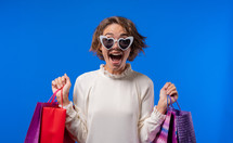 Excited woman with colorful paper bags after shopping on blue studio background. Concept of seasonal sale, purchases, spending money on gifts