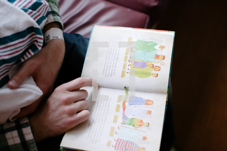 father reading a Children's Bible to a newborn baby 