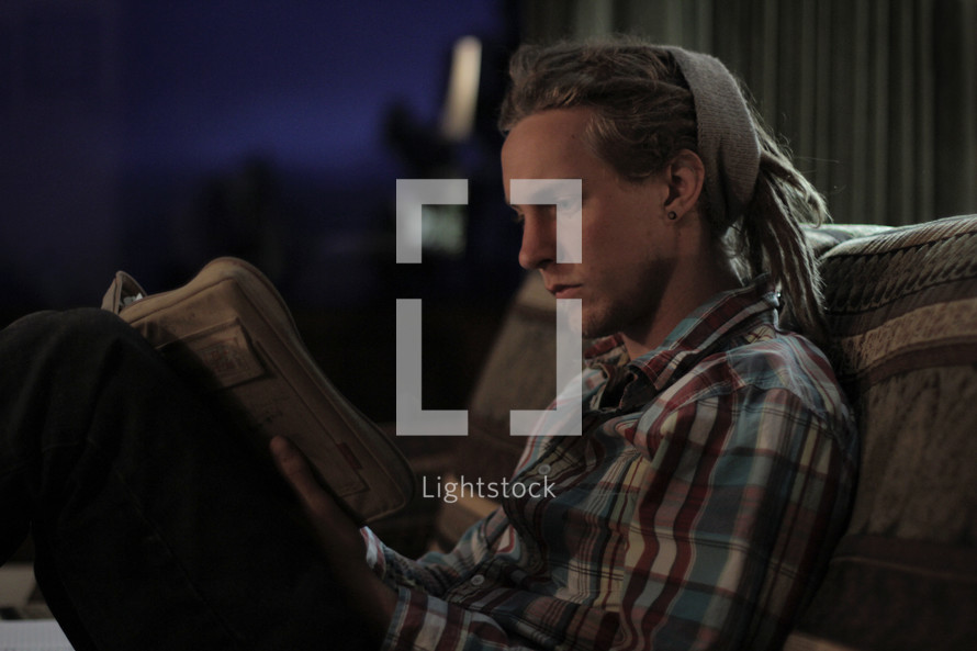 man with dreads sitting on a couch reading a Book 