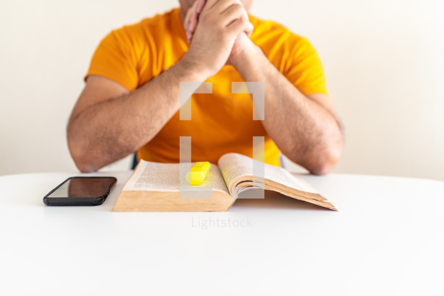 a man with praying hands reading a Bible 