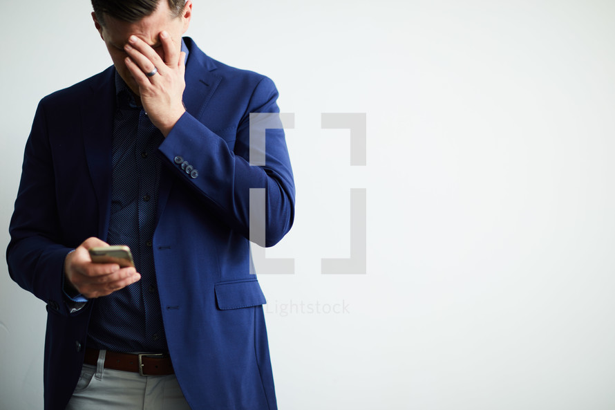 a man looking down at his cellphone covering his face with his hand 