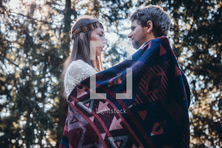 a couple wrapped in a blanket standing in a forest 