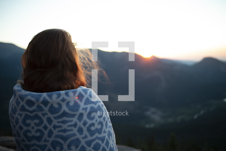 girl wrapped in a blanket watching the sunrise on a mountaintop 