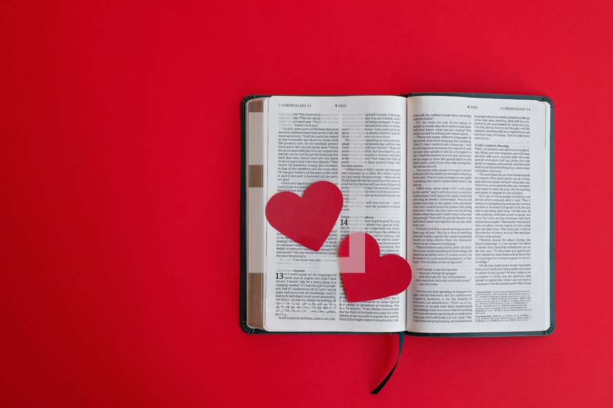 Two red hearts on an open Bible with a red background and copy space