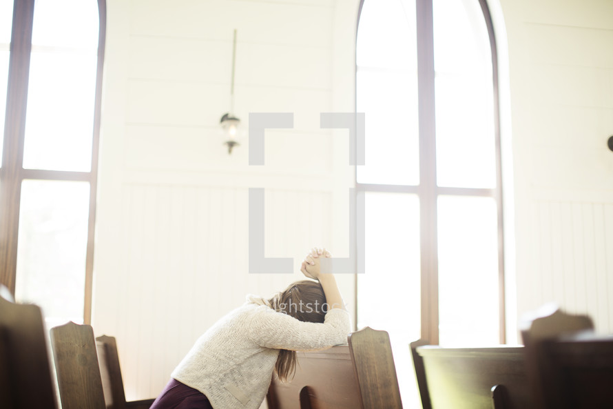 a woman praying sitting in a church pew 