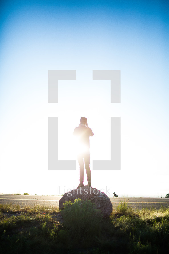 Sunshine on a man standing on a round boulder.