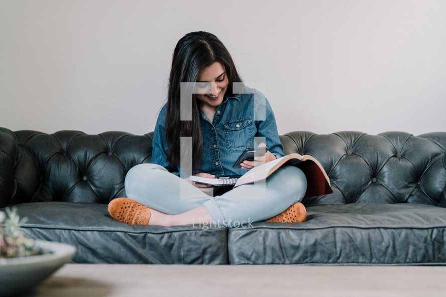 a woman sitting on a couch reading a Bible and taking notes in a journal 
