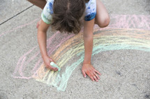 a child drawing a rainbow with sidewalk chalk 