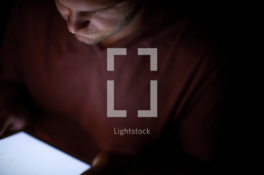 A man's face illuminated by the light from an electronic tablet.