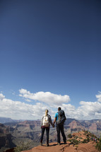 man and woman standing at the edge of a canyon cliff holding hands  