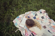woman sitting outdoors reading a book lying on a blanket 
