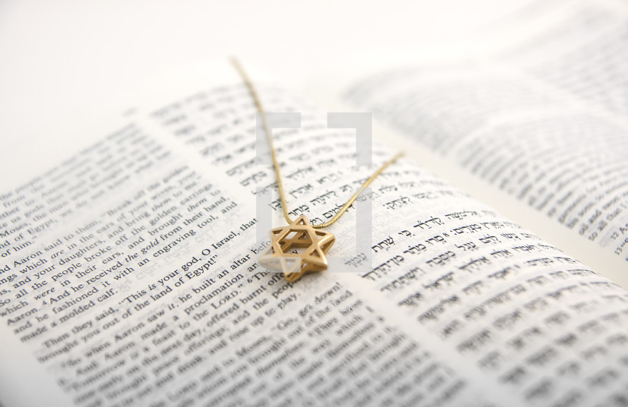 Open Hebrew/English Bible with a gold Star of David pendant on the page.