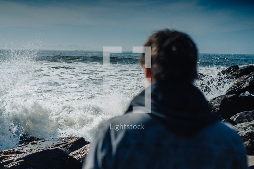 man standing on a shore looking out at the ocean 