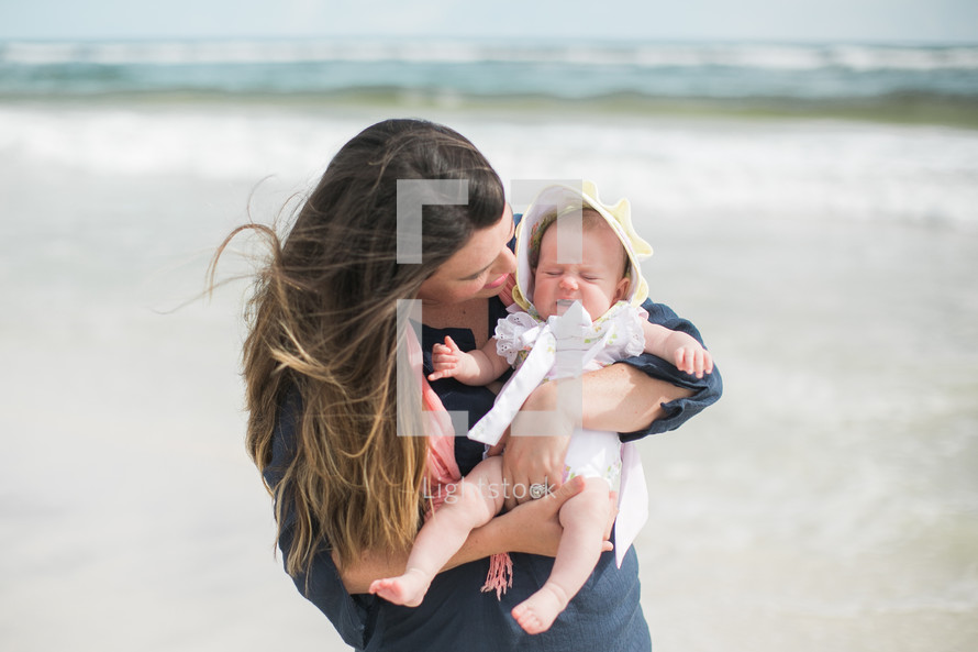 a mother holding her baby daughter on a beach 