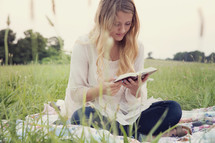 woman sitting on a blanket in the grass reading a Bible 