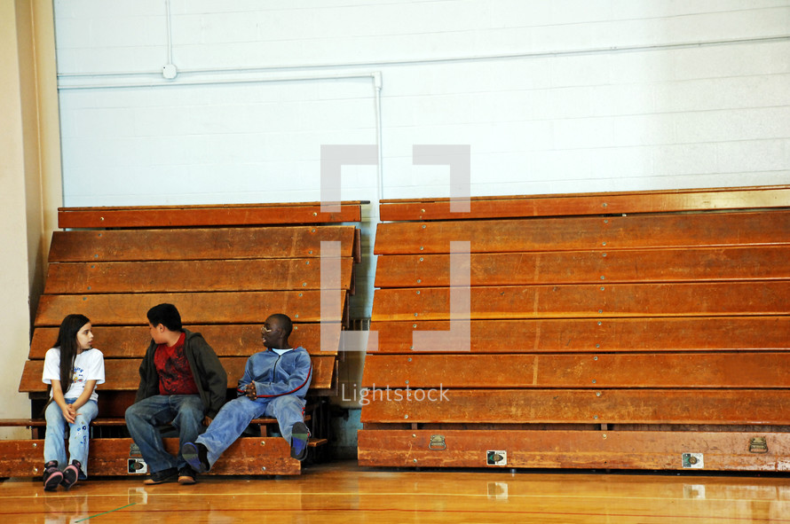 teens sitting on bleachers in a gymnasium 