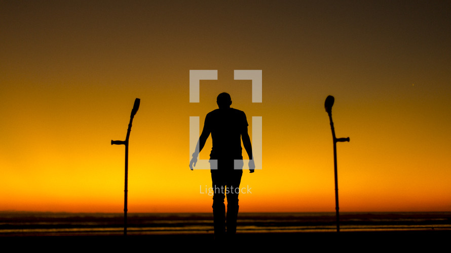 silhouette of a man standing and crutches 