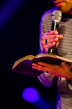 man reading a Bible speaking into a microphone 