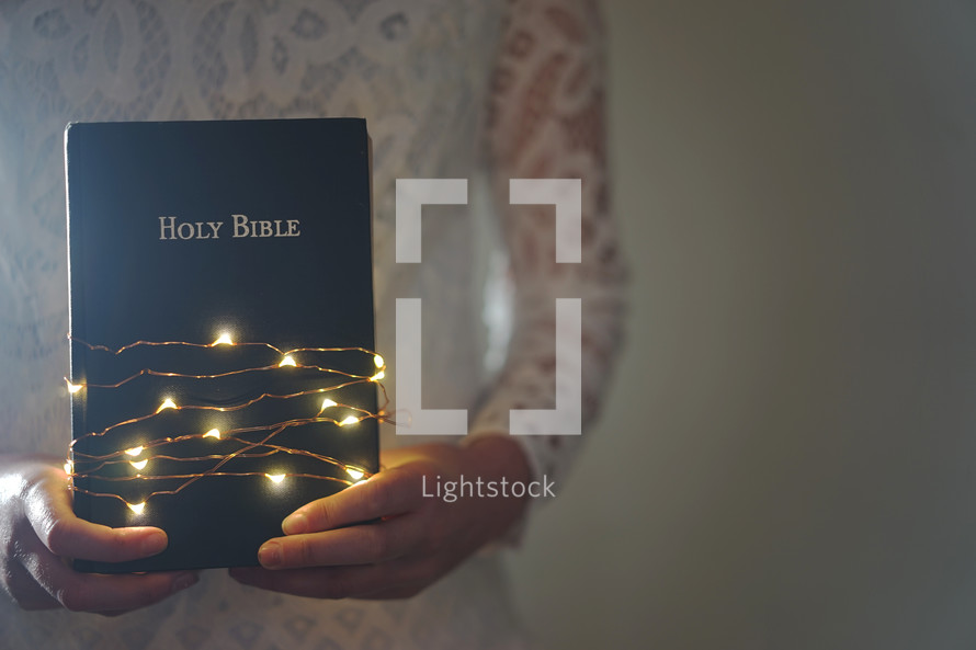 a woman holding a Bible wrapped in Christmas lights 