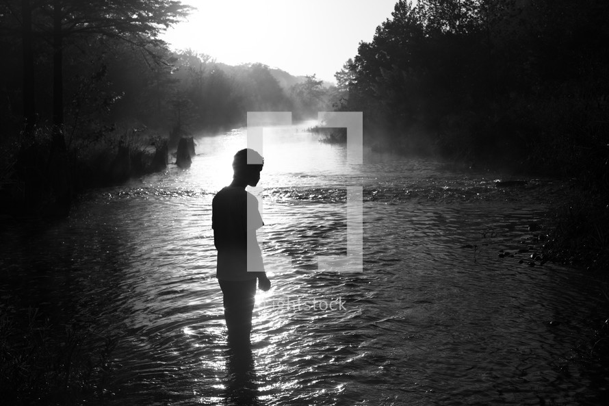 a silhouette of a young man standing by a river 