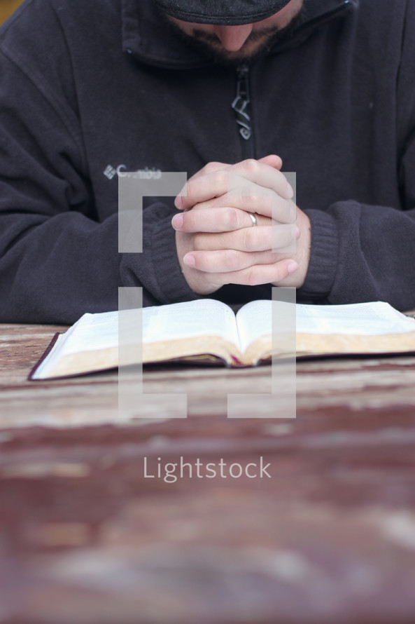 man with praying hands over the pages of a Bible 