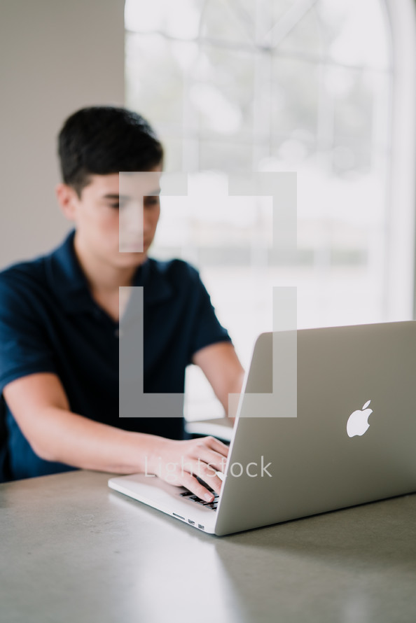 a teen boy typing on a laptop computer 