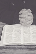 praying hands over the pages of a Bible 