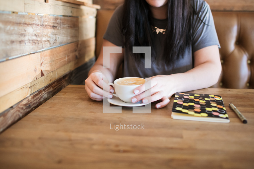 a girl with a journal and coffee cup sitting at a table