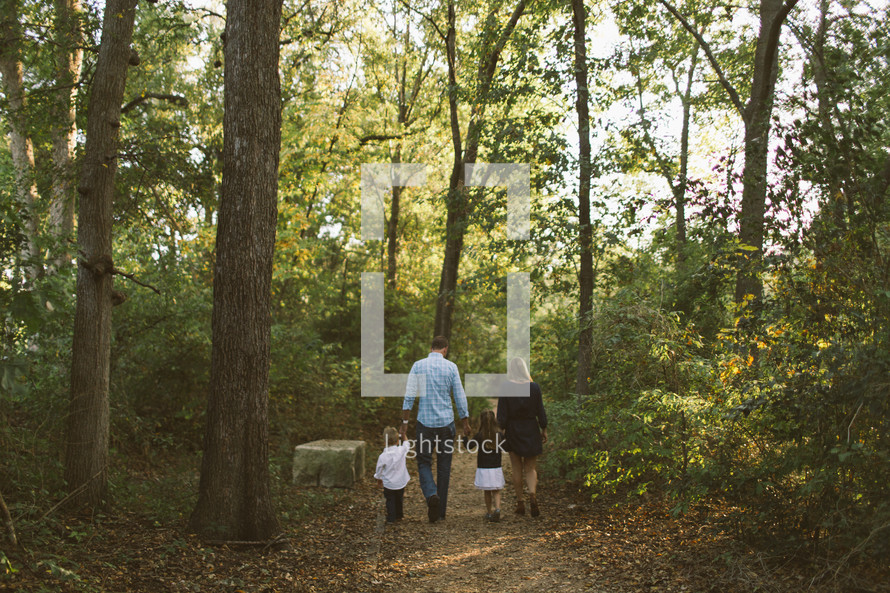 a family walking through the woods along a trail holding hands 