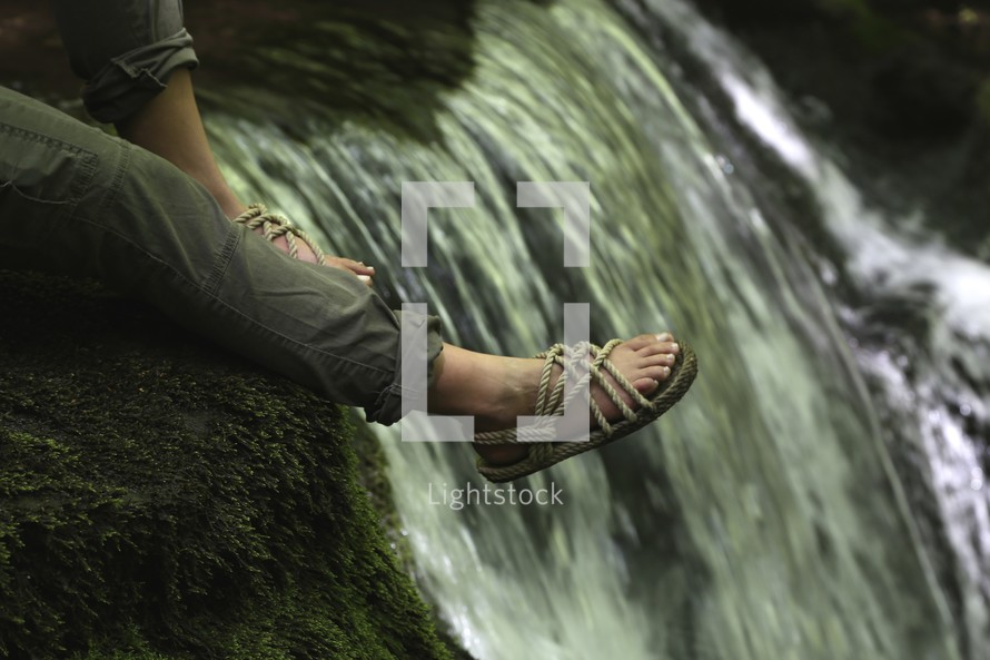 feet hanging over an edge near a waterfall 