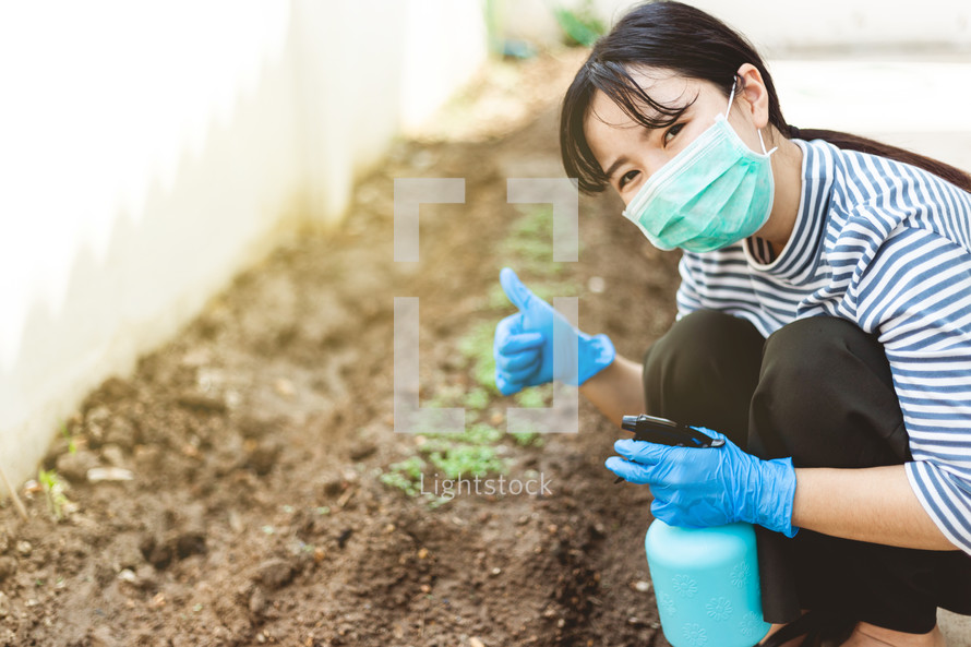 a woman watering a garden wearing a mask 