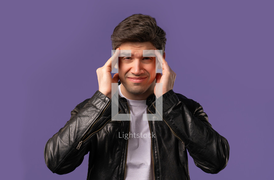 Young man having headache, blood pressure, studio portrait. Guy putting hands on head, isolated on violet background. Concept of problems, medicine, illness. High quality