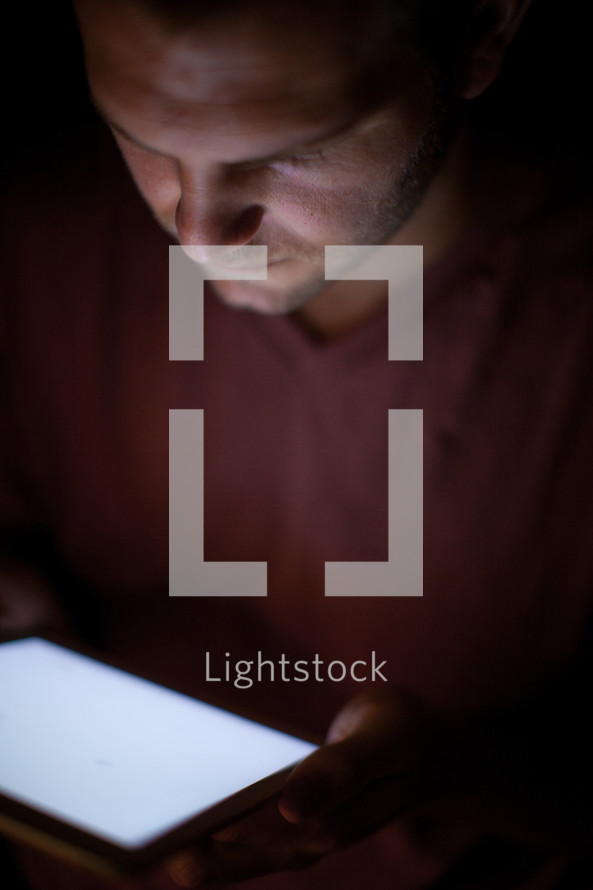 A man's face illuminated by light from an electronic tablet.