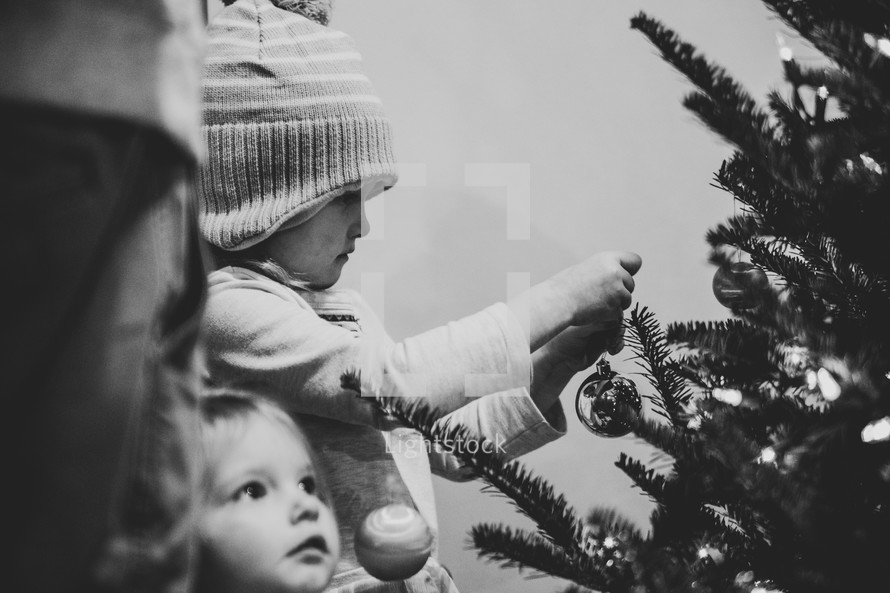 Small children hanging ornaments on a Christmas tree - black and white