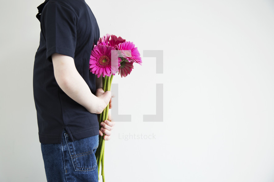 A boy holding flowers behind his back.