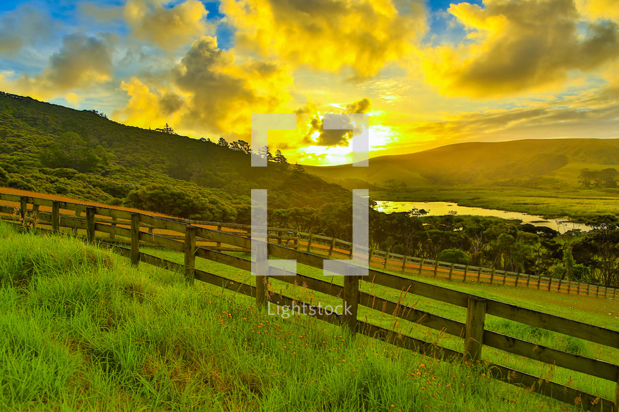 sunrise over a green pasture and fence line 