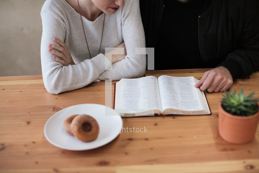 couple reading a Bible and donuts on a plate 